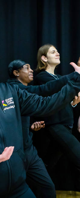A lecturer and students striking dramatic poses against a black curtain, smiling and enjoying their creative acting activity. A lecturer and students striking dramatic poses against a black curtain, smiling and enjoying their creative acting activity.